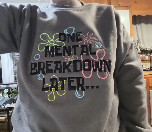 Charcoal gray embroidered crewneck sweatshirt reading One Mental Breakdown Later with colorful outlined accents